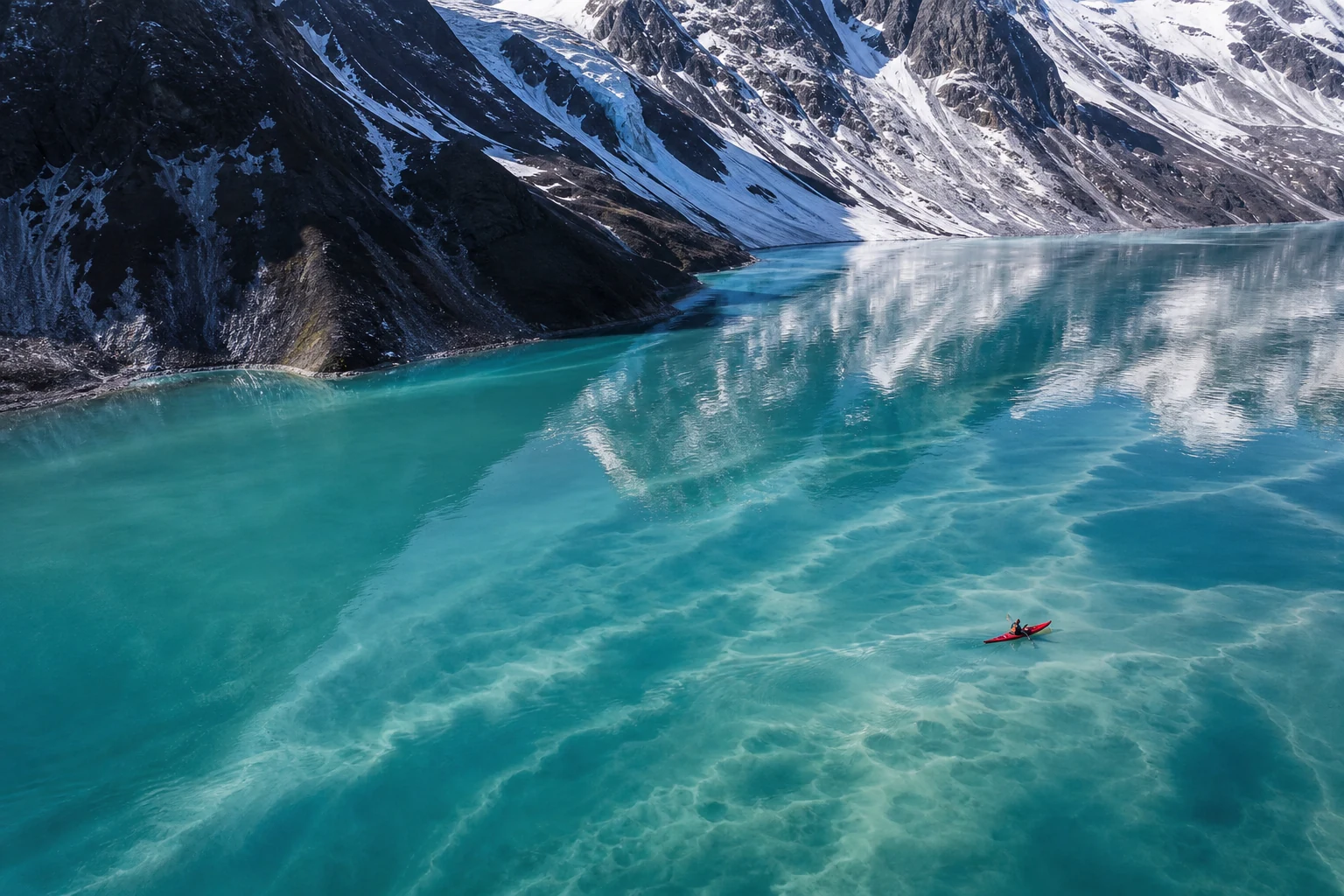 Red kayak crossing a turquoise glacial lake beneath snowy mountains